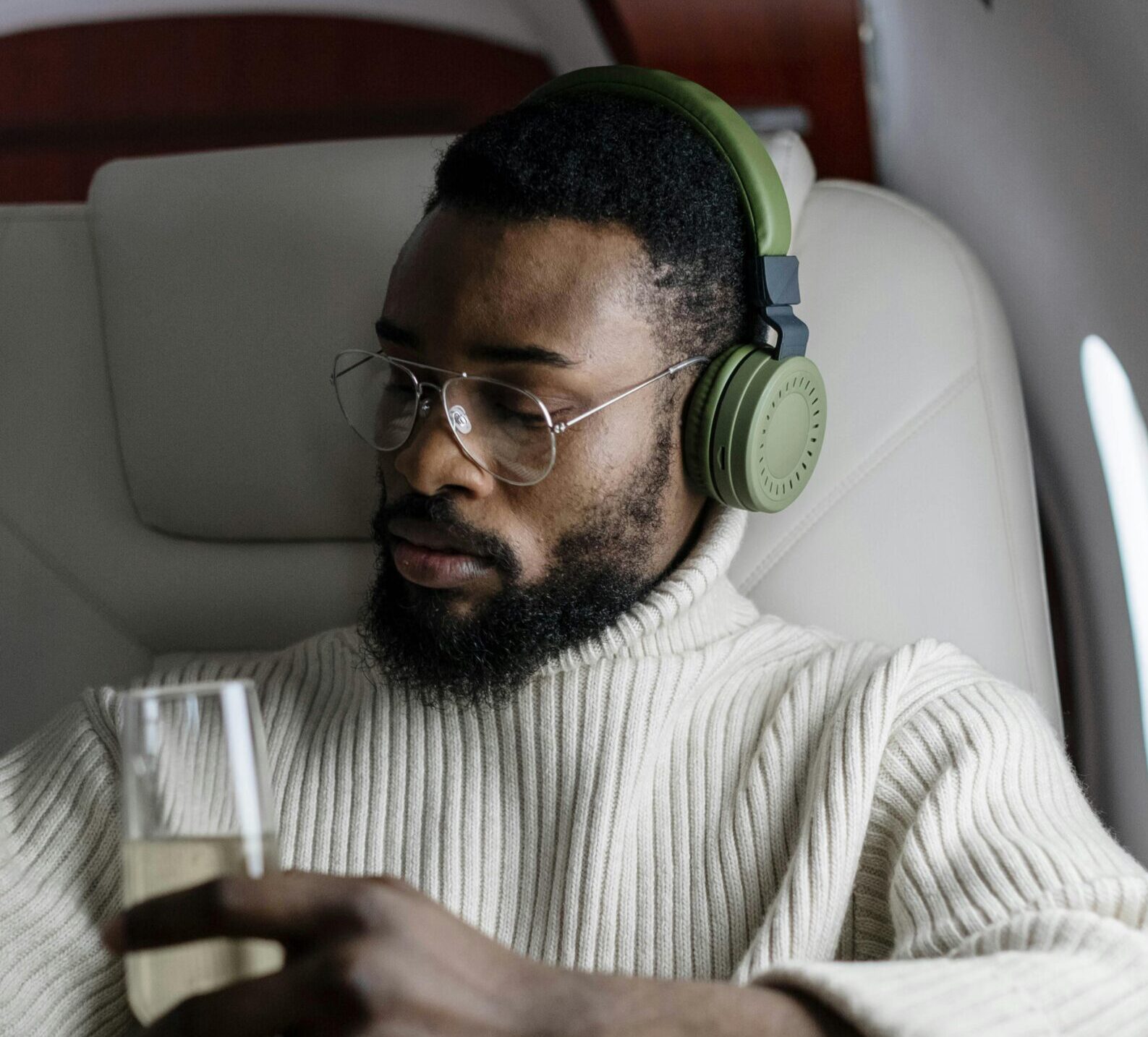 Man in sweater with headphones sipping champagne on a private jet, conveying luxury and relaxation.